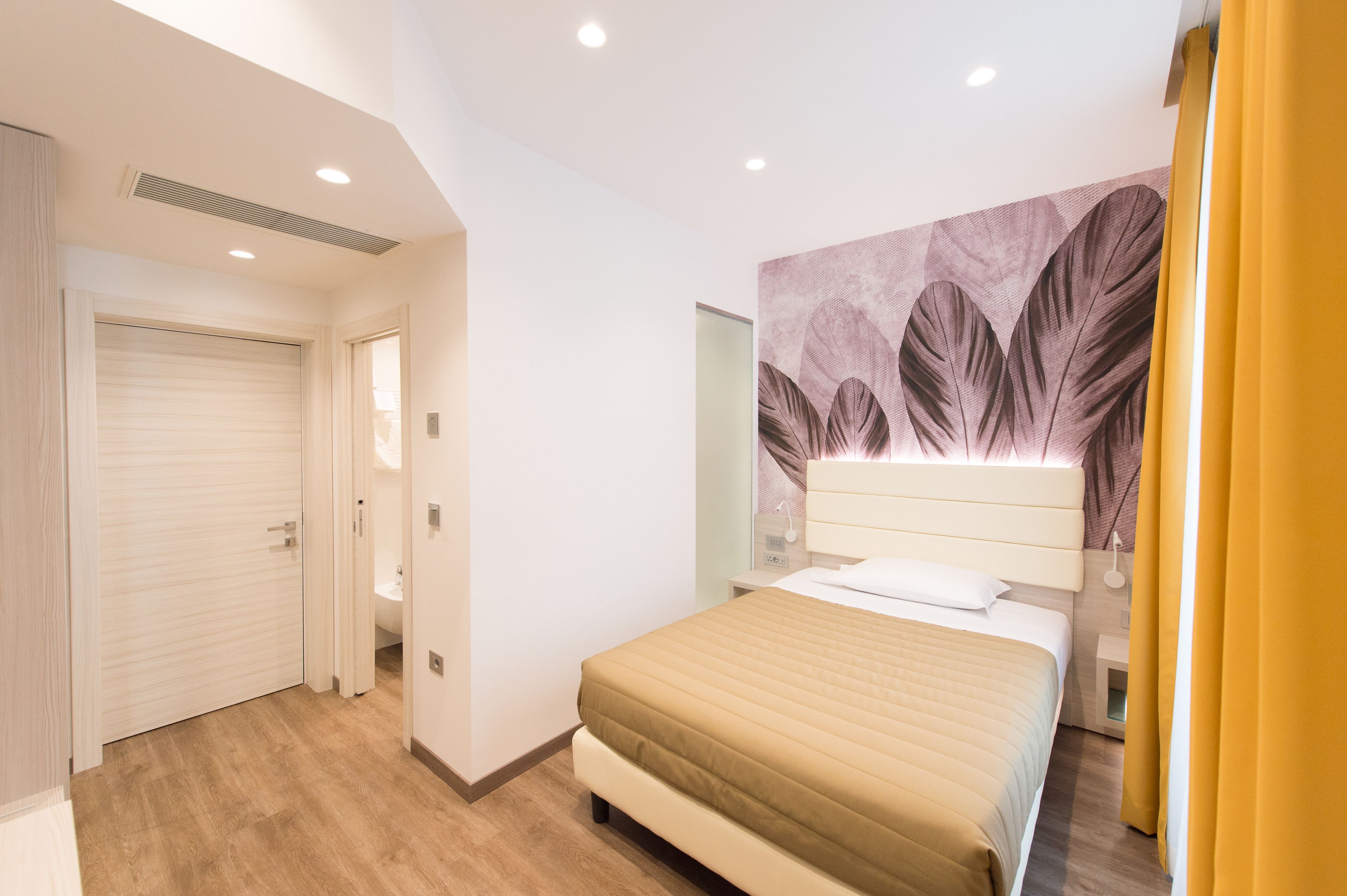 Un dormitorio con cama, cabecera con diseño de hojas, mesita de noche y puerta que da a un baño.