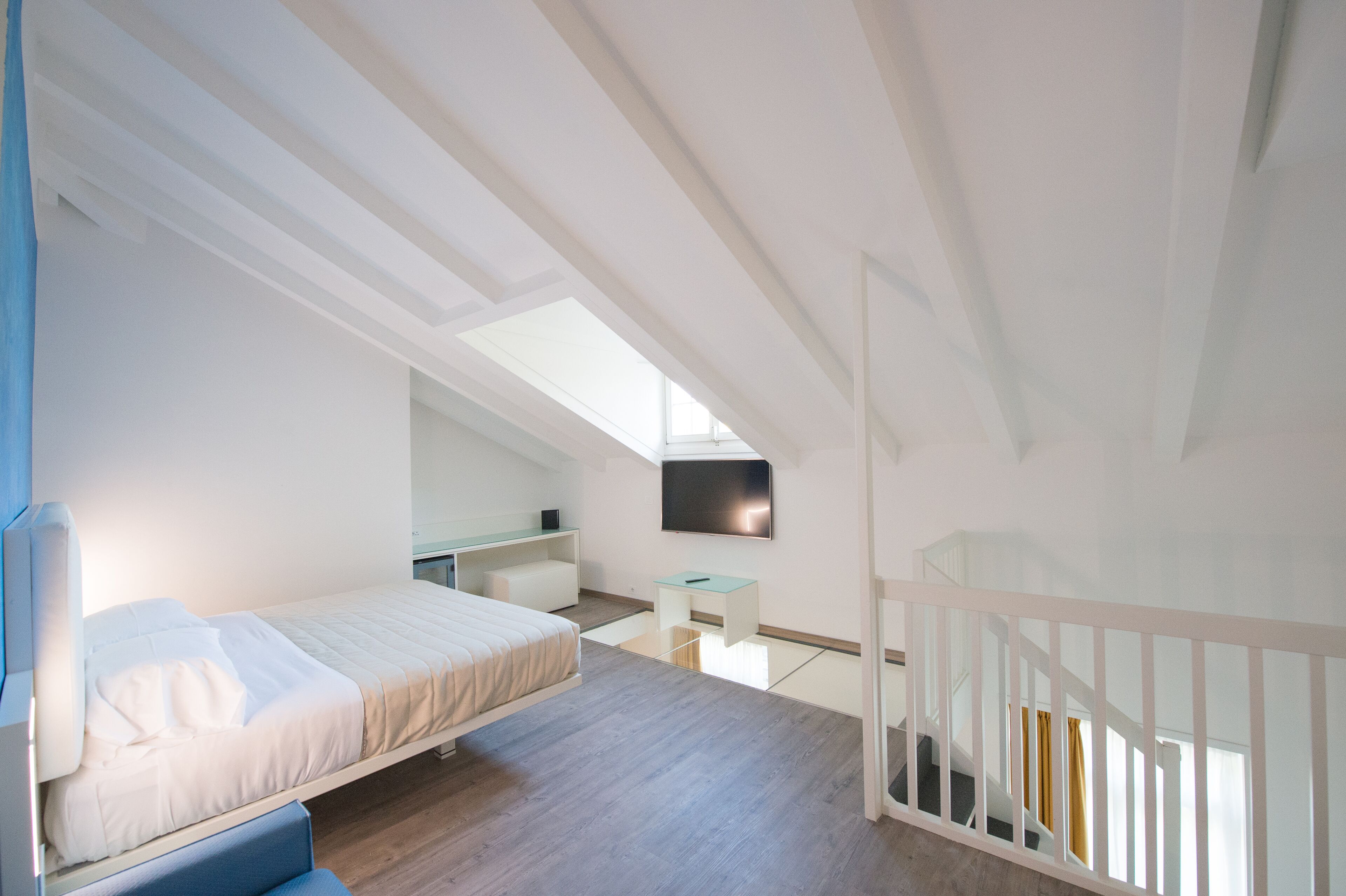A modern, well-lit bedroom with a bed, a desk, and a TV mounted on the wall.