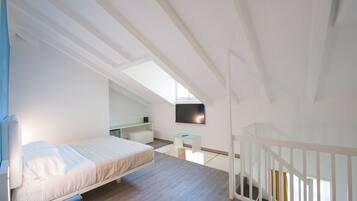 Ein modernes, gut beleuchtetes Schlafzimmer mit einem Bett, einem Schreibtisch und einem an der Wand montierten Fernseher.