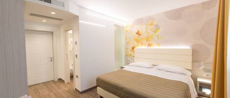 Quarto de hotel com cama, mesa de cabeceira e banheiro visível através de uma porta aberta.