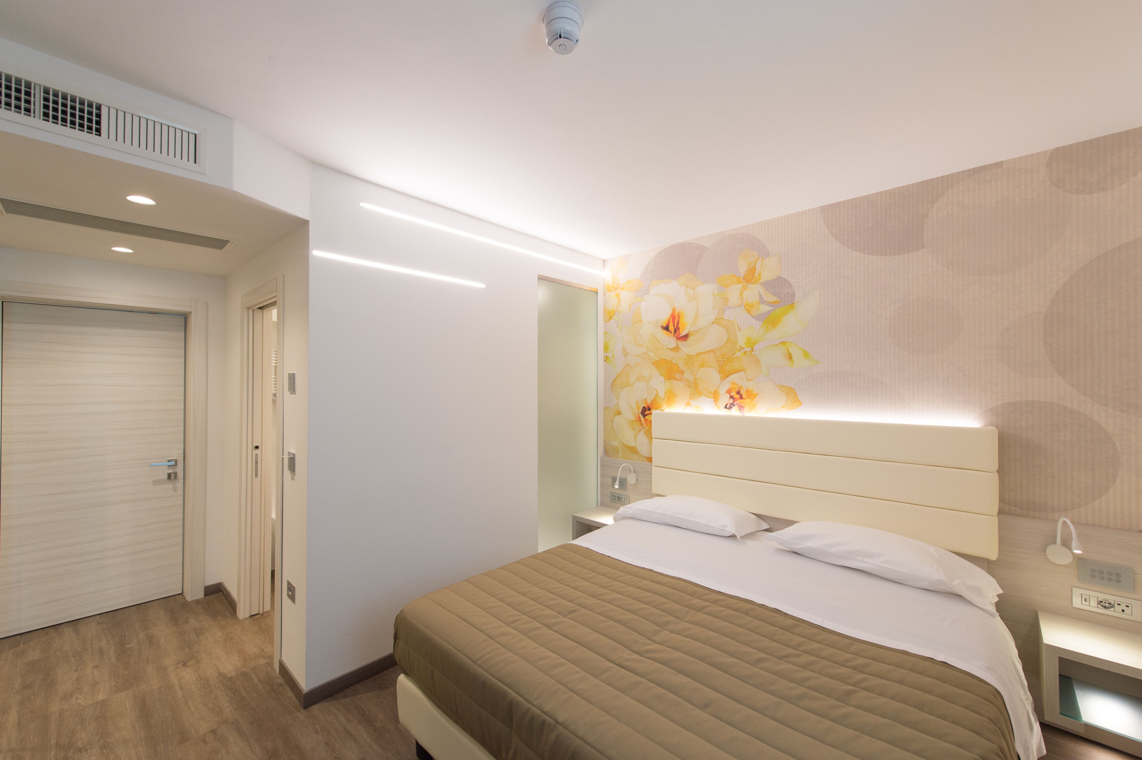 A hotel room with a bed, bedside table, and a wall-mounted light fixture.