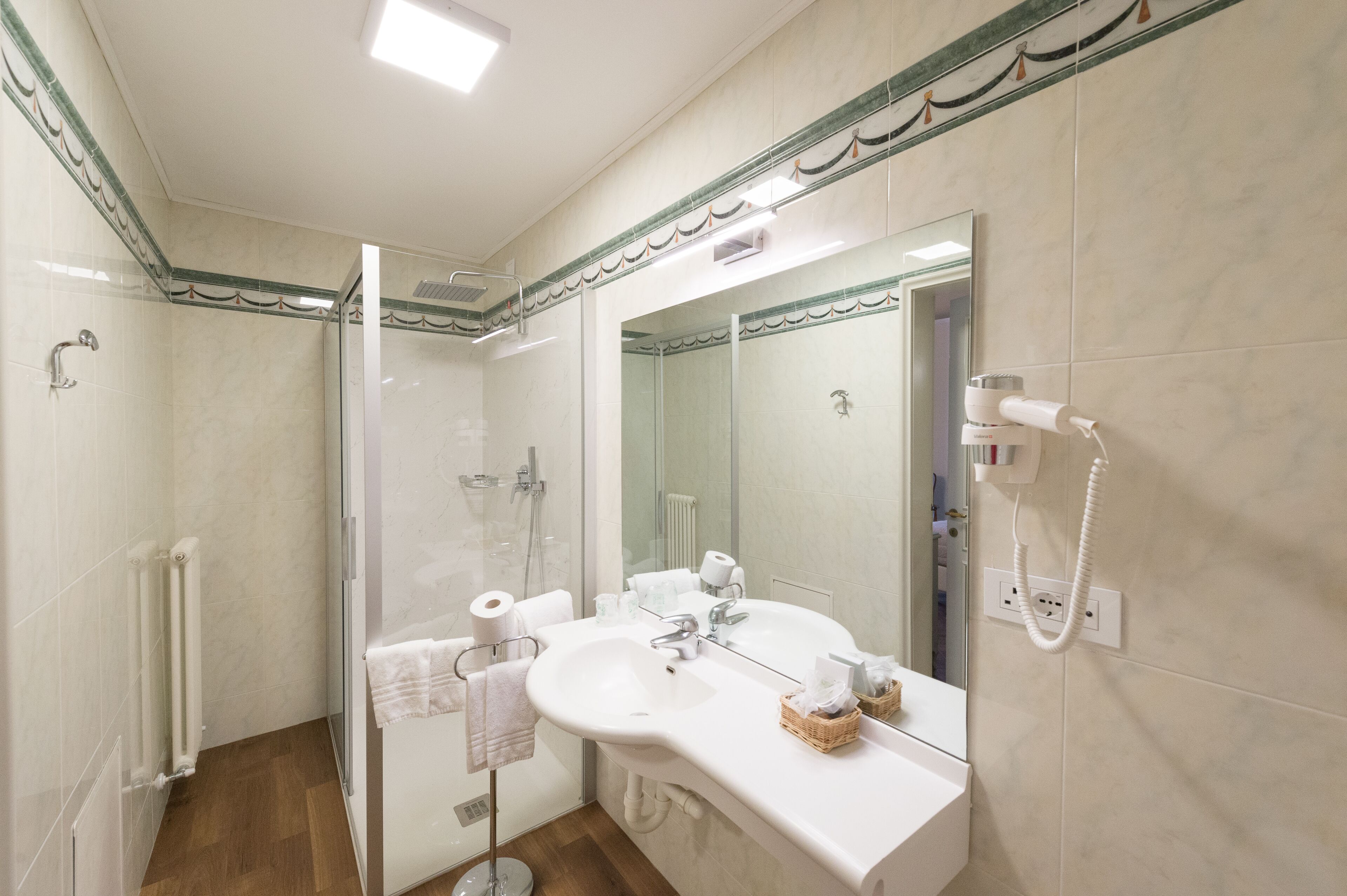 Un baño moderno con ducha envuelta en vidrio, un espejo grande y un lavamanos blanco con toallero.