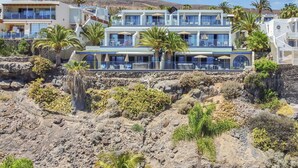 Ein mehrgeschossiges Hotel mit Außenbereich und Palmen, eingebettet in eine felsige Hügelkulisse.