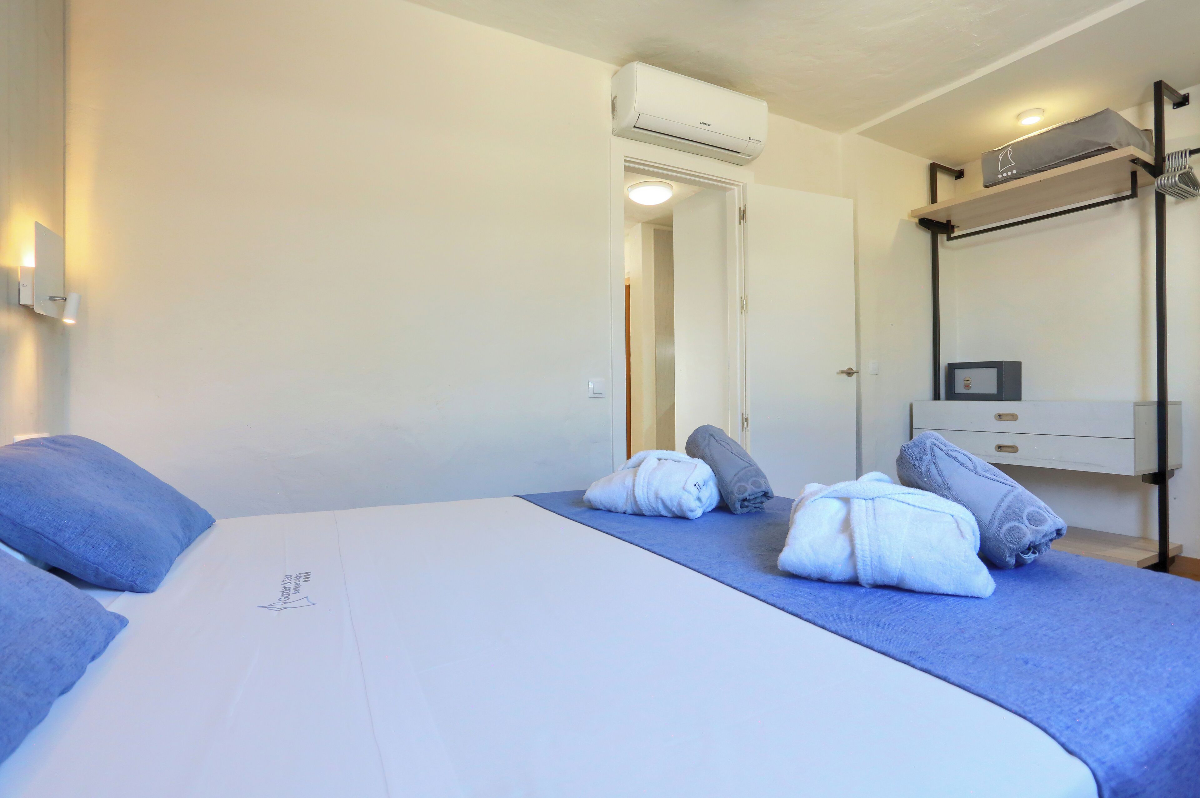 Ein Hotelzimmer mit Bett, Handtüchern, einer Klimaanlage, einem Nachttisch, einem Spiegel und einem am Wand montierten Fernseher.