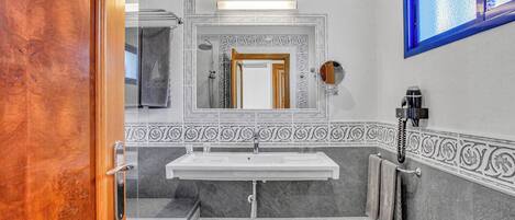A bathroom with a white sink, a mirror, a towel rack, and a shower.