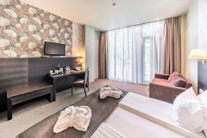 A hotel room with a bed, a desk, a chair, a TV, and a window with curtains.