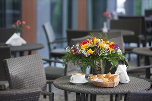 A round table with a white cup, a basket of croissants, and a floral arrangement.