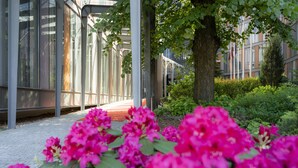 Un bâtiment moderne doté de grandes fenêtres en verre, d’un chemin et d’une végétation luxuriante agrémentée de fleurs roses.