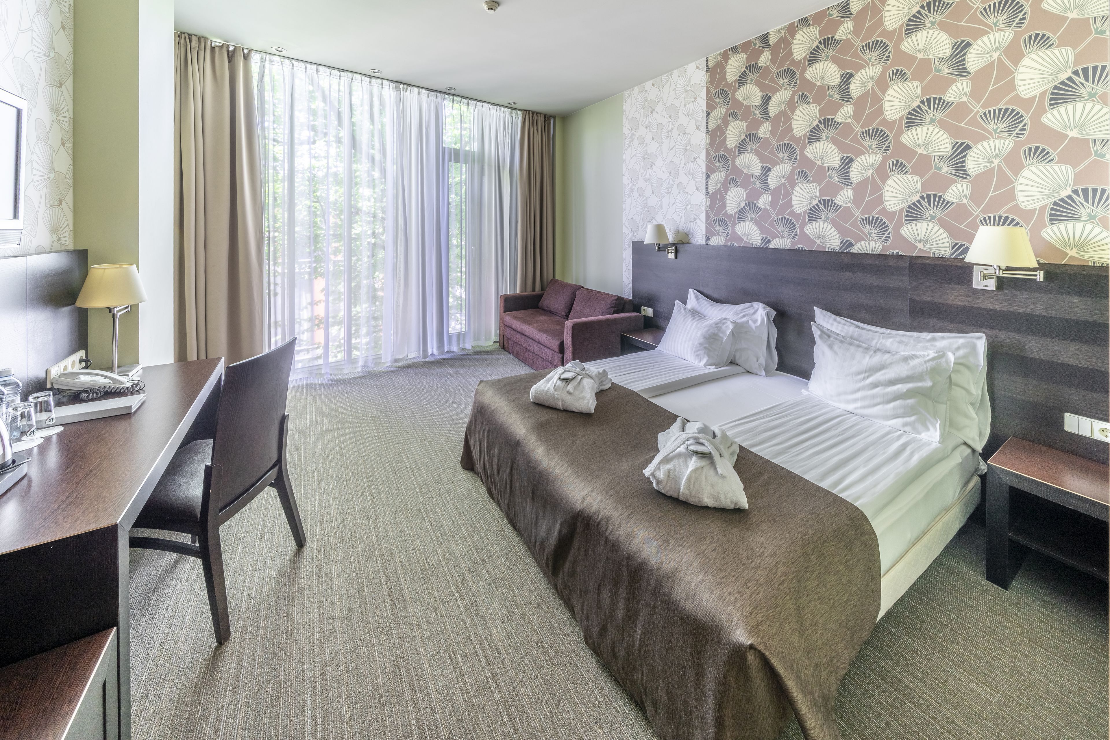 A hotel room with a bed, a desk, a chair, and a sofa.
