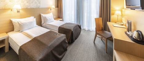A hotel room with two beds, a desk, a chair, a television, and a window with curtains.
