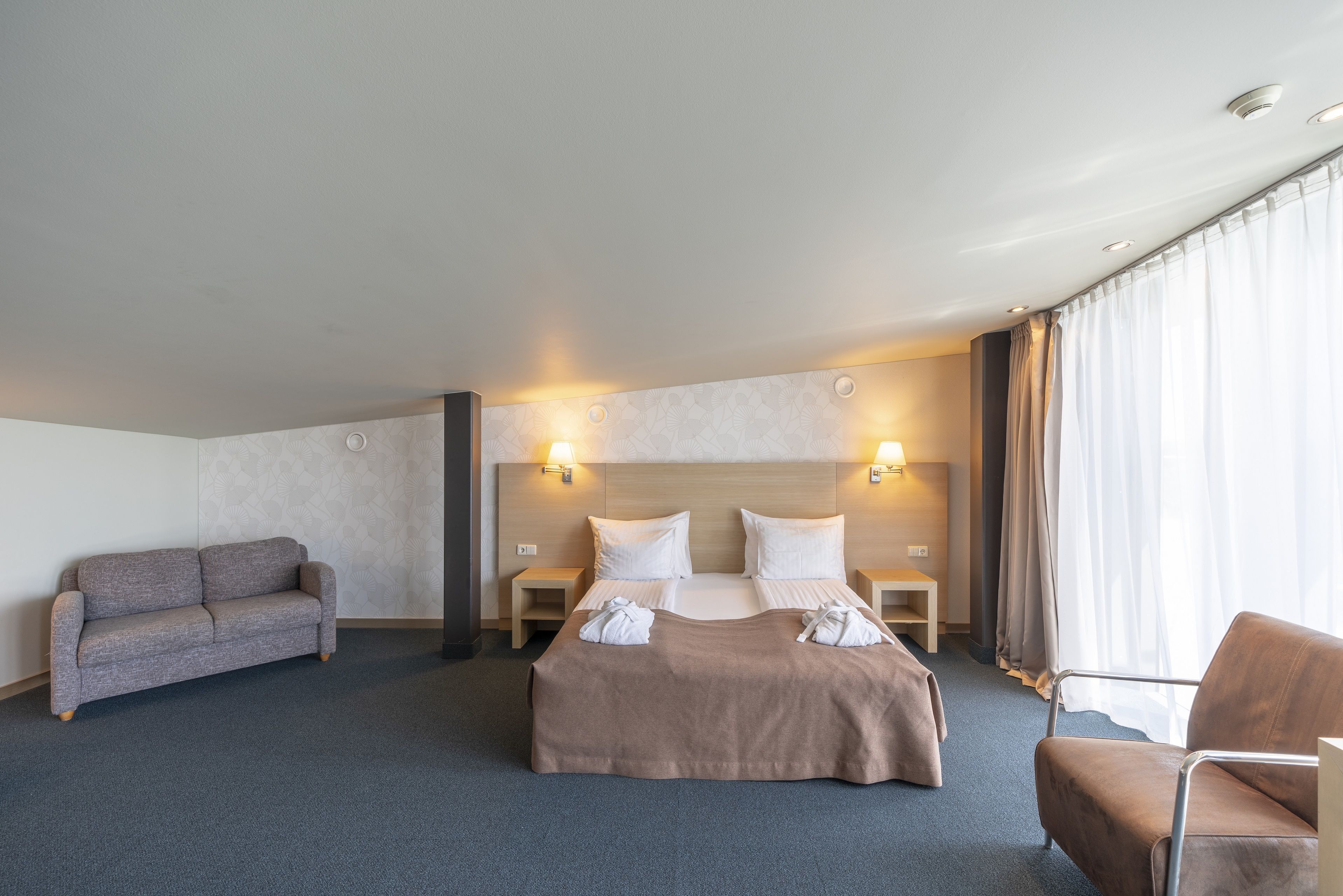 A hotel room with a bed, two bedside tables, a sofa, and a chair.