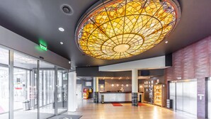 Un hall d’hôtel doté d’un grand plafond en vitrail, d’un comptoir d’accueil et d’une entrée en verre.