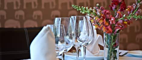 Ett matbord dukat med genomskinliga glas, en vit servett och en vas med färgstarka blommor.