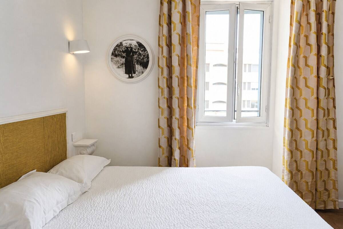 A hotel room with a bed, a round wall decoration, a window with curtains, and a wall-mounted light.