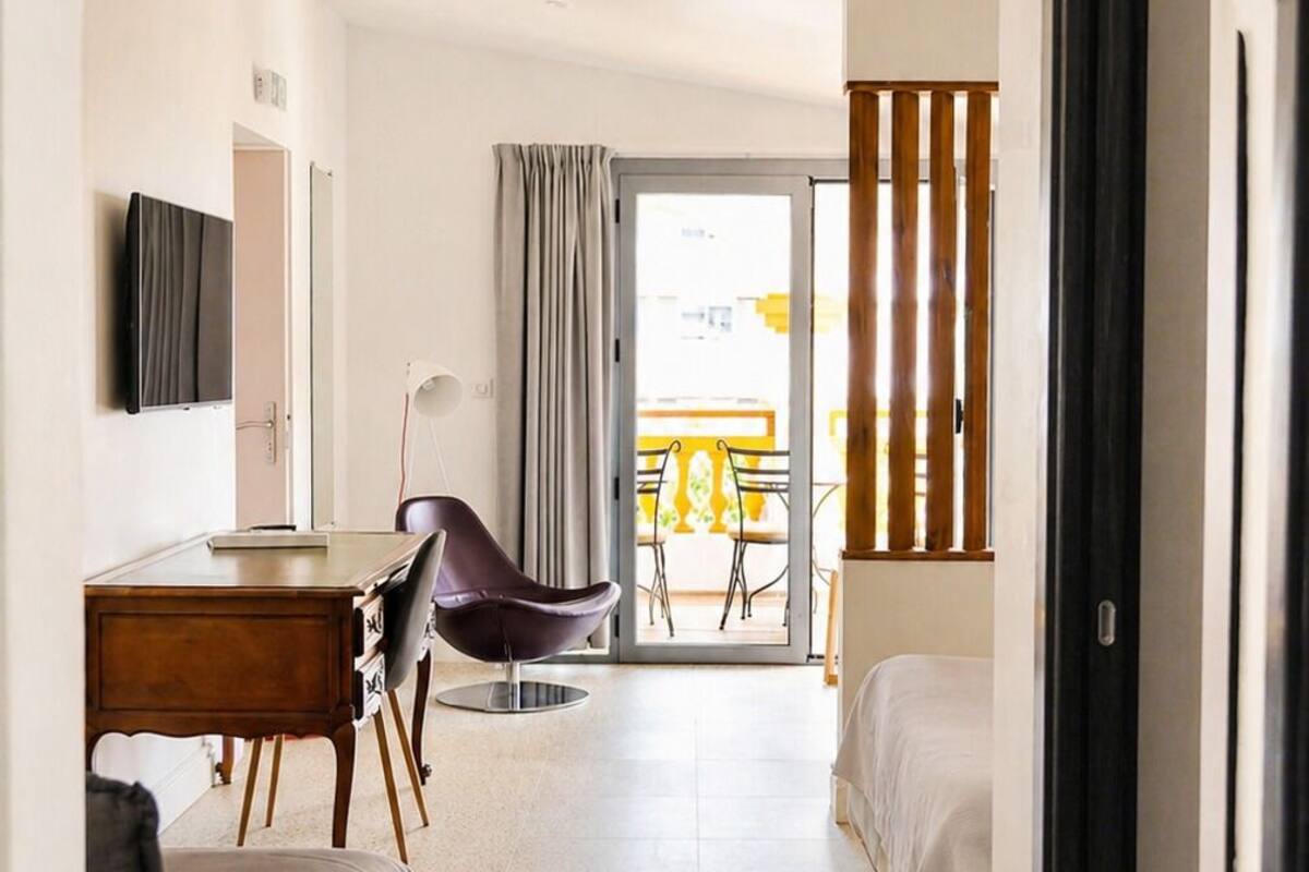 A hotel room with a bed, a desk, a chair, a TV, and a balcony with a table and chairs.