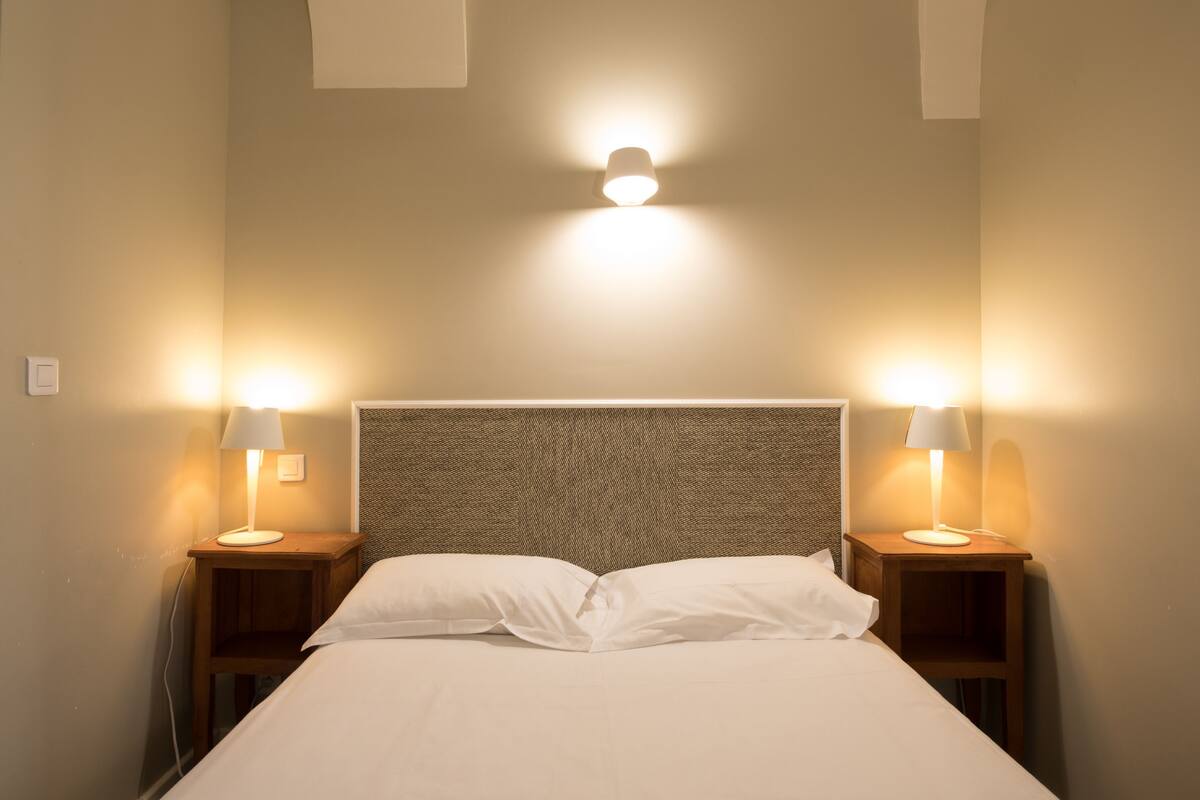 A neatly made bed with white linens, two bedside lamps, and a wall-mounted light fixture.