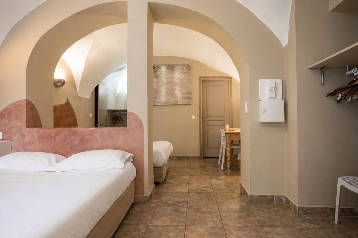 A hotel room with a bed, a desk, and a chair. There is a door leading to another room.