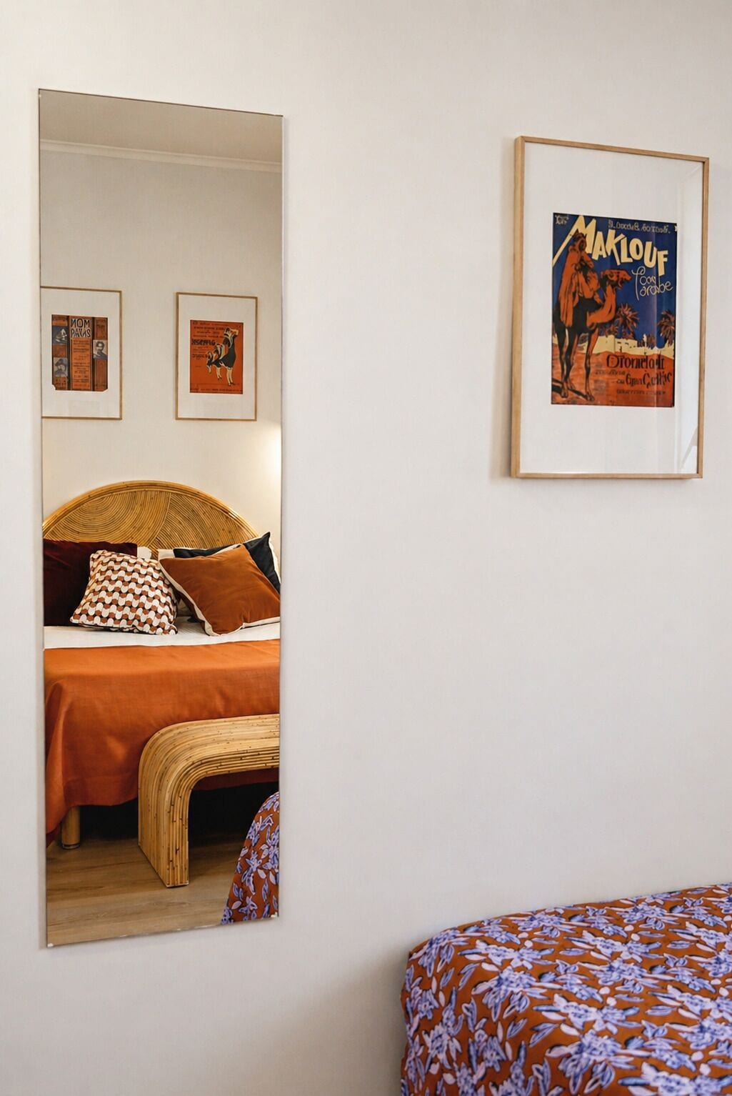 A bedroom with a bed, a mirror, and framed posters on the wall.