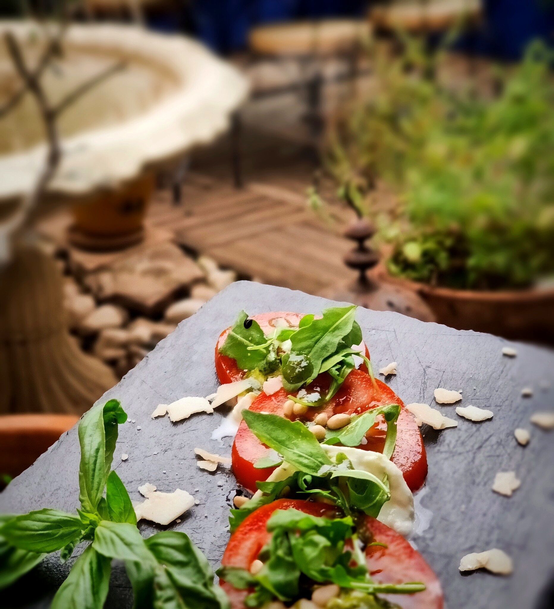Primer plano de una ensalada de tomate con albahaca y queso rallado sobre una bandeja de pizarra.
