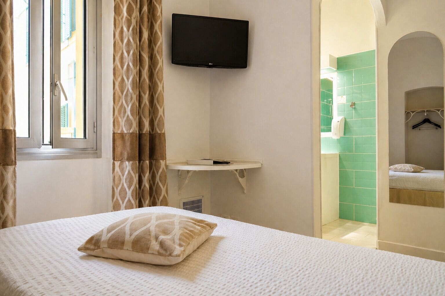 Un dormitorio con cama, televisor montado, mesita de noche y baño visible a través de un arco.