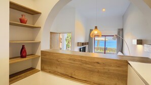 Een modern interieur met houten planken, een houten toonbank en uitzicht op zee door een boogvormige doorgang.