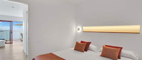 Een moderne hotelkamer met een groot bed, een plafondventilator, een balkon met uitzicht op zee en een heldere, aan de muur bevestigde lamp.