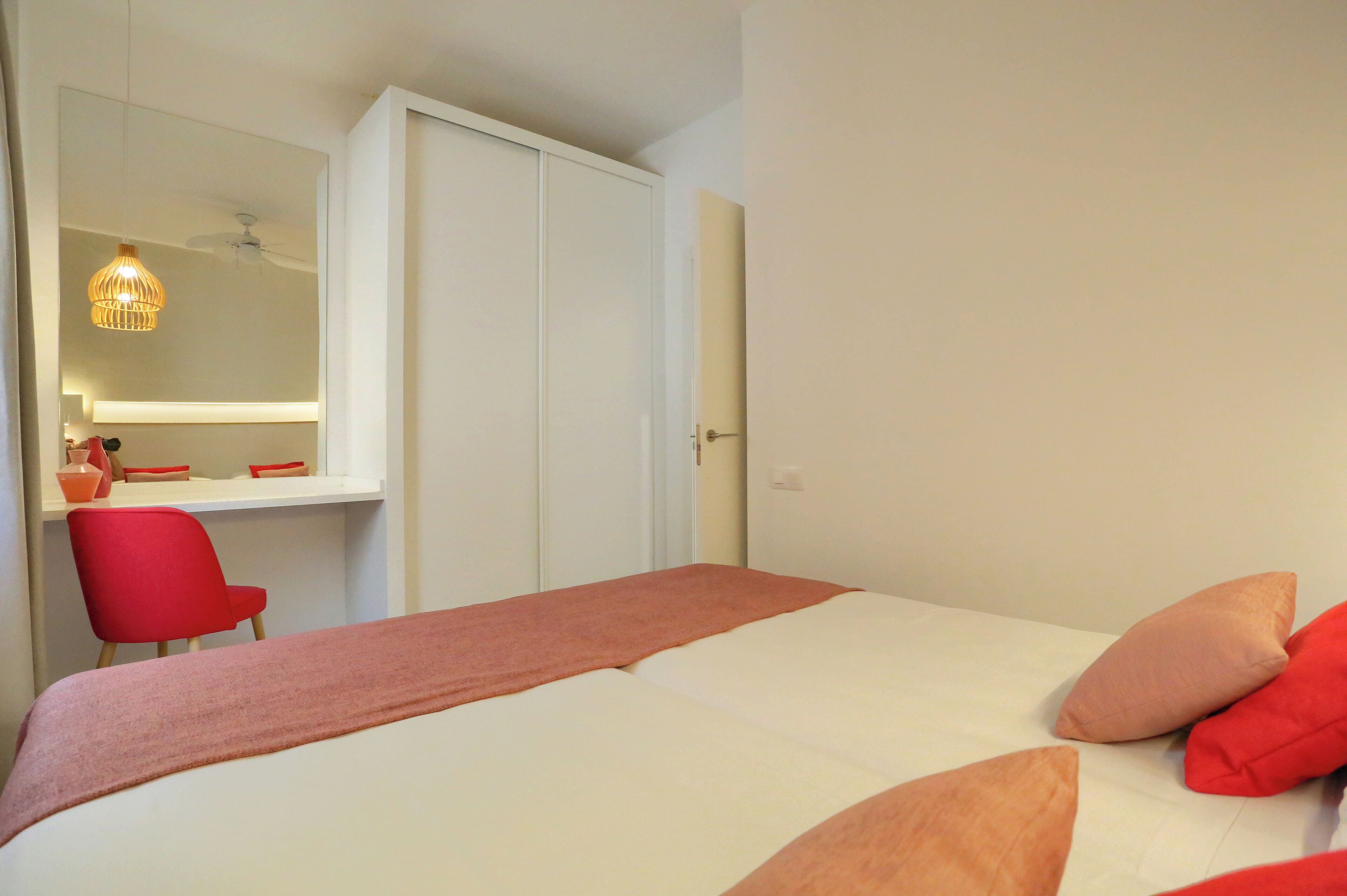 A bedroom with a bed, a red chair, a desk with a mirror, and a wardrobe.