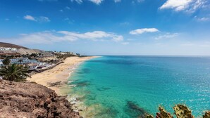 Vista costeira com praia arenosa, águas turquesa cristalinas e um escarpe rochoso.