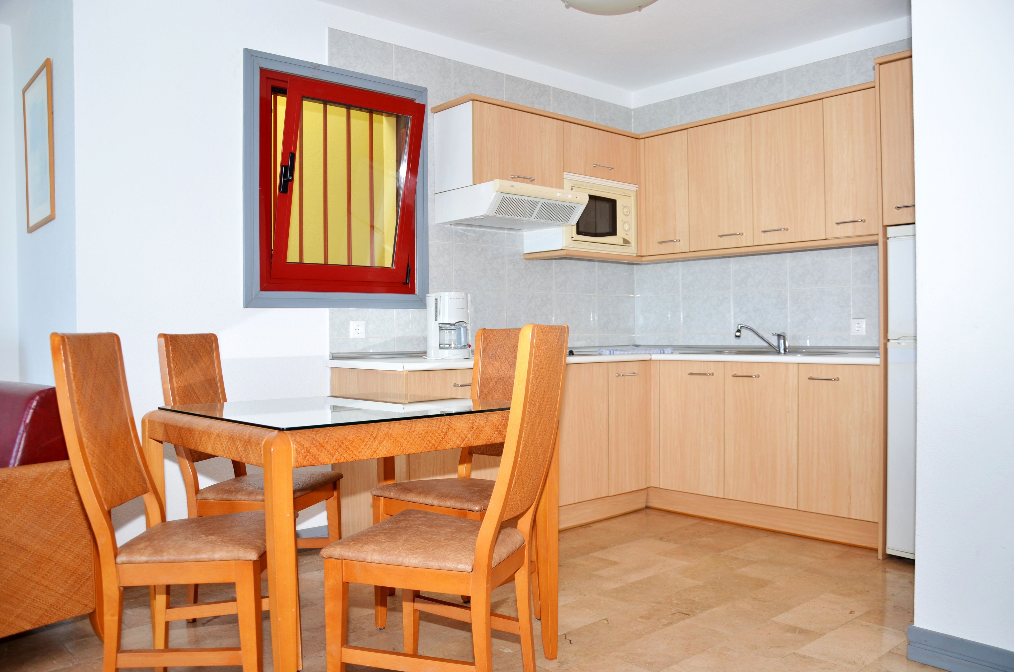 A compact kitchen with wooden cabinets, a microwave, and a dining area with a glass table and chairs.