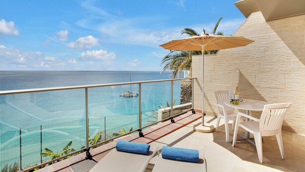 Een balkon met een helder uitzicht op zee, een tafel met stoelen en een parasol.