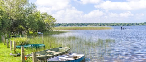 A calm lake with boats docked on the grassy shore, surrounded by trees and a clear sky.