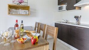 Una cocina moderna con armarios oscuros, un microondas y una mesa de comedor de madera dispuesta con copas de vino, pan y un bol de fruta.