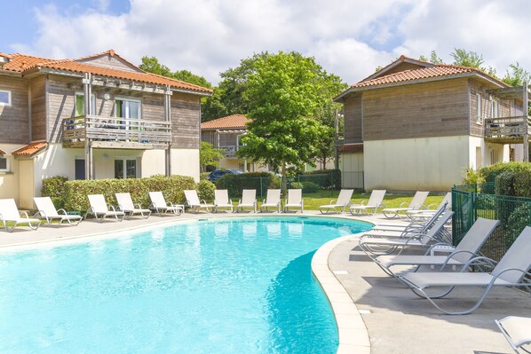 Una piscina con sillones de descanso y un edificio de madera con balcón.