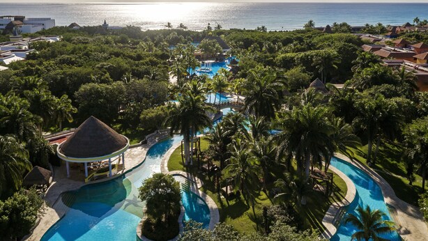 A resort with a large pool area, palm trees, and a view of the ocean.