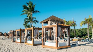 A beach with wooden cabanas, each with a thatched roof and white curtains.