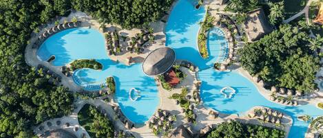 Eine Vogelperspektive zeigt ein Resort mit mehreren Schwimmbecken, umgeben von üppiger Vegetation und Palmen.
