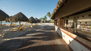 A beachside bar area with wooden deck, thatched umbrellas, and lounge chairs.