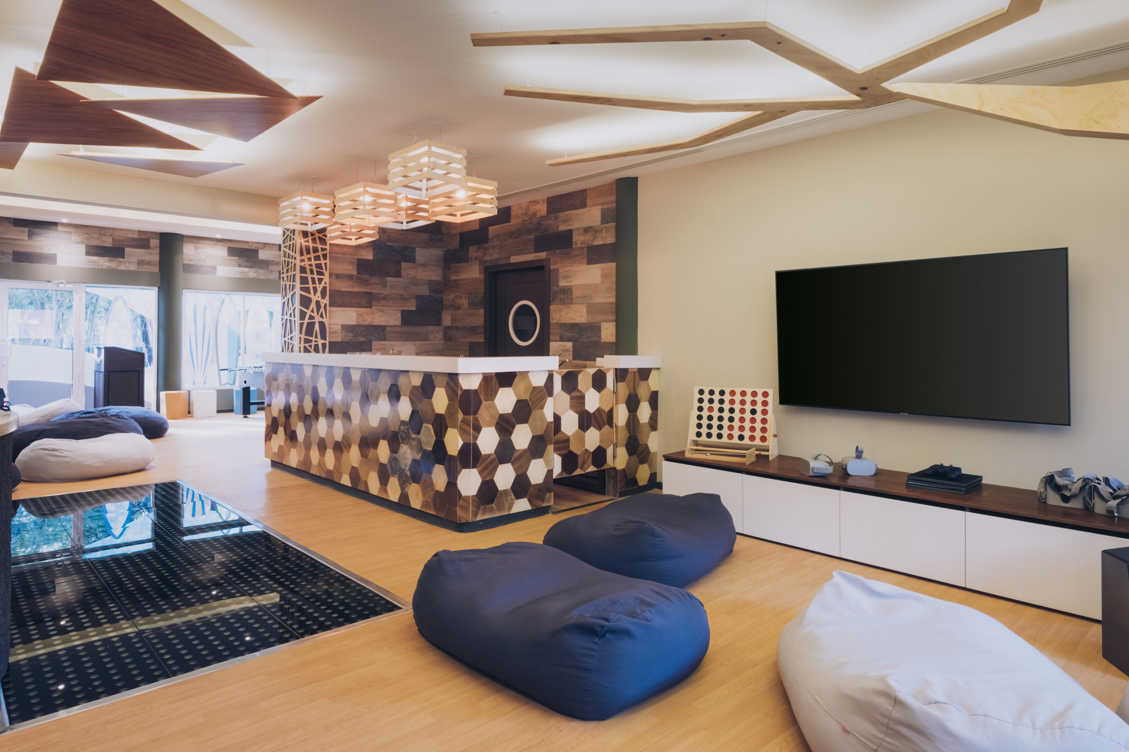 A modern living room with a wooden floor, a central seating area with blue and white cushions, a built-in entertainment unit with a flat-screen TV, and a unique wooden wall design.