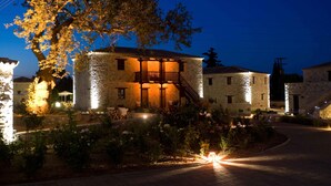 A stone building with a balcony and a staircase, surrounded by a garden with flowers and a paved walkway. - Semantron Traditional Village (Aigialeia)