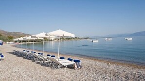 A beach with rows of sun loungers and white tents, a calm sea, and boats in the distance. - Semantron Traditional Village (Aigialeia)