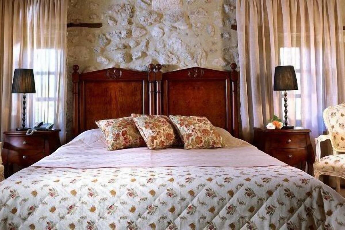 Een slaapkamer met een groot bed, beddengoed met bloemenprint, twee nachtkastjes met lampen en een stenen muur.