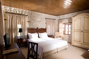 Un dormitorio con techo de madera, paredes de piedra, una cama con ropa de cama blanca, un escritorio con ordenador, una silla y un armario.