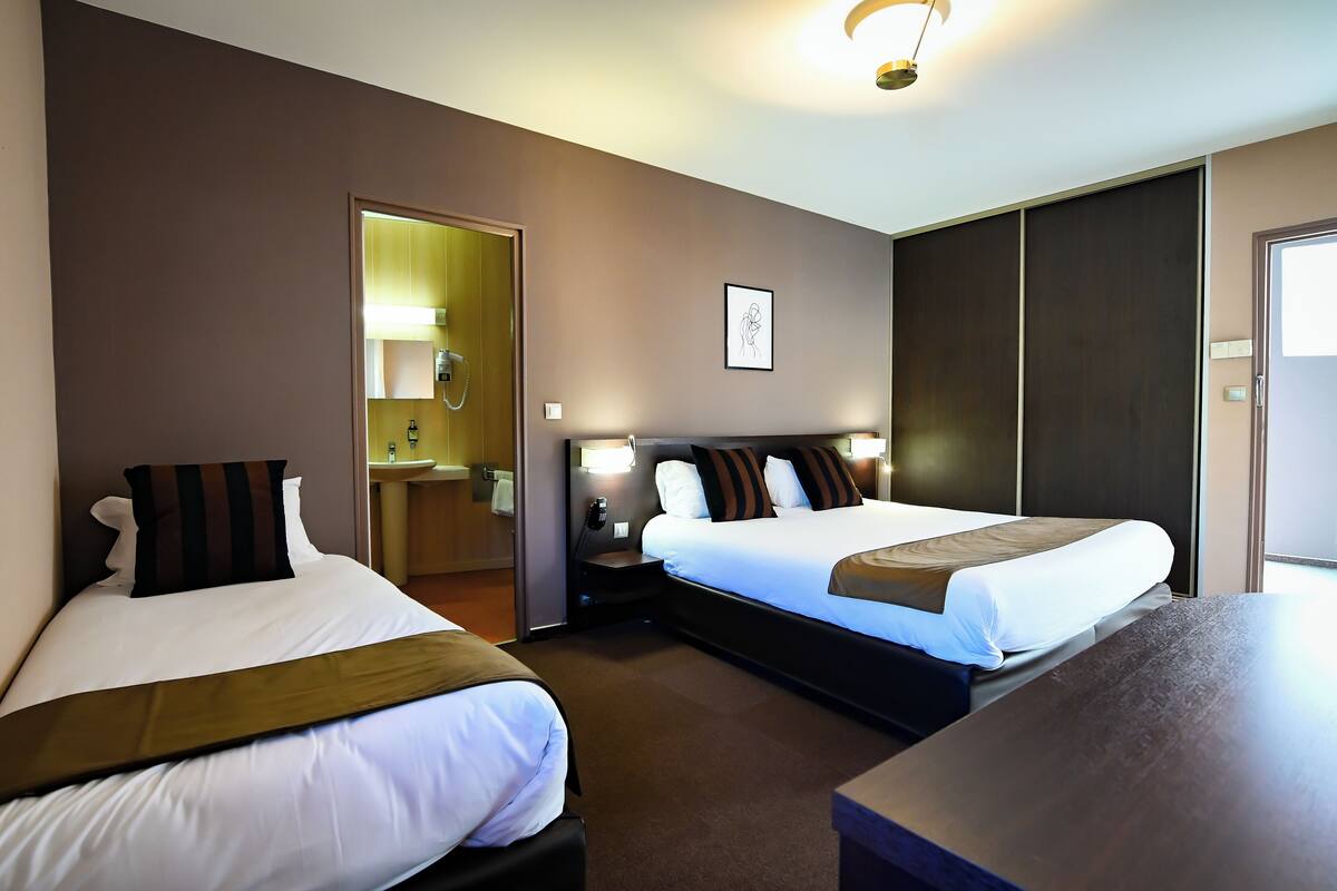 Une chambre d’hôtel avec deux lits, un bureau, un miroir et une porte donnant sur une salle de bain.