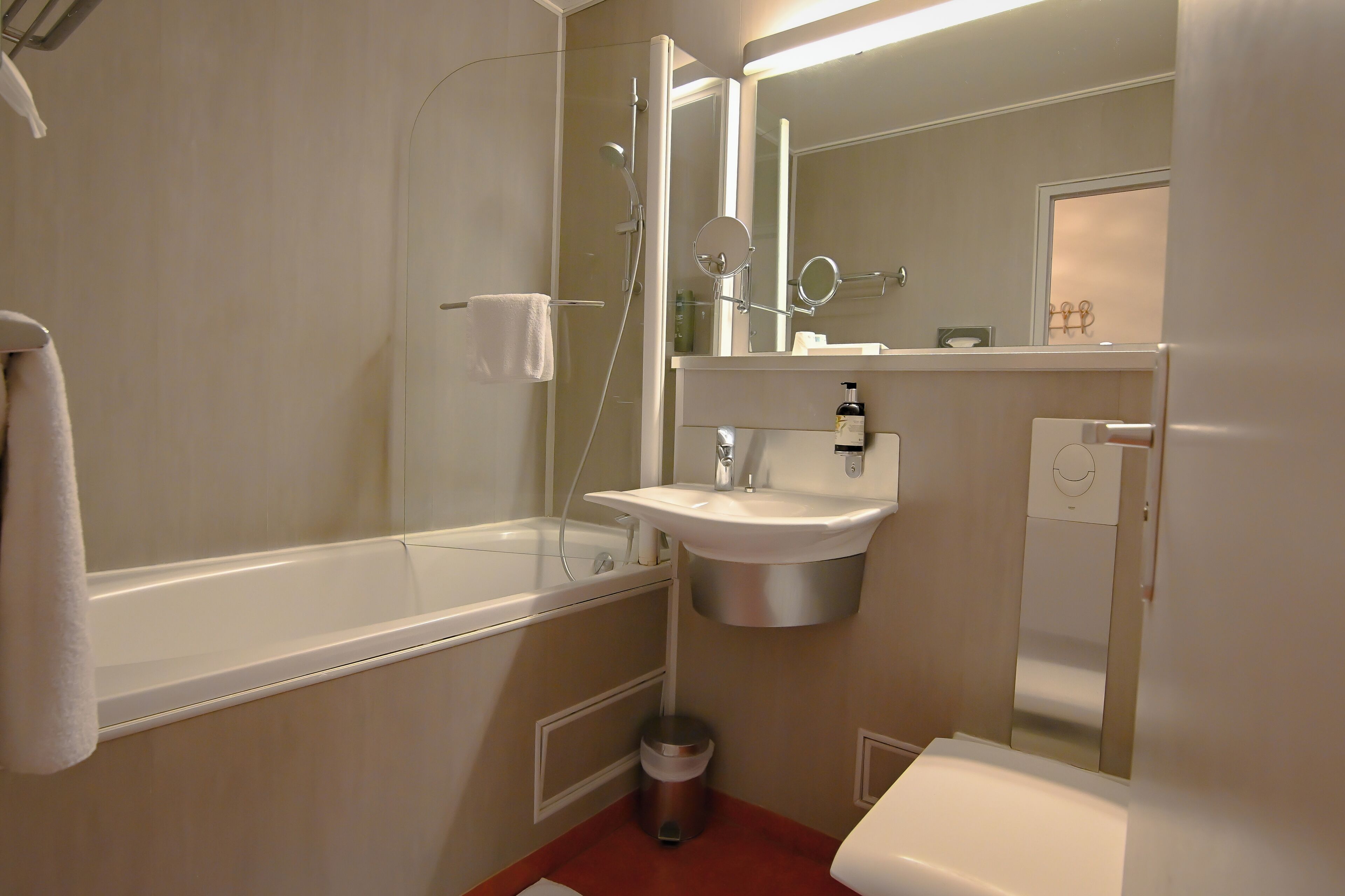 A bathroom with a bathtub, sink, mirror, and a trash bin.
