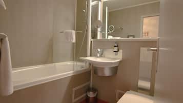 A bathroom with a bathtub, sink, mirror, and a trash bin.