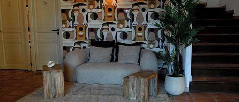 Un espacio de estar con un sofá, dos mesitas de madera, una planta en maceta y un papel tapiz decorativo.