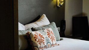 Un lit bien fait, agrémenté d’oreillers à motifs, une lampe de chevet et un téléphone posé sur la table de nuit.