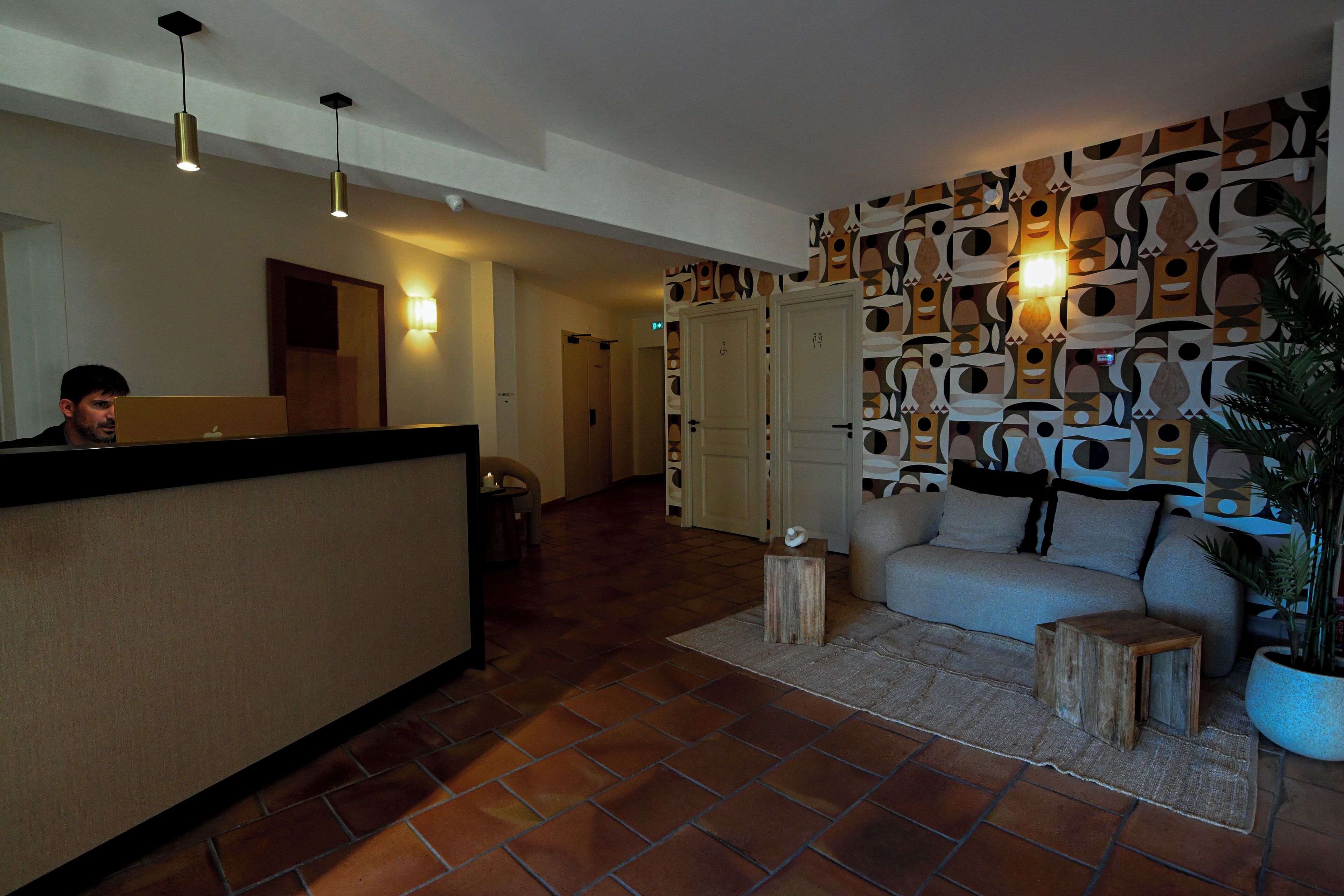 Un área de recepción con mostrador, sofá, planta en maceta y pared con diseño.