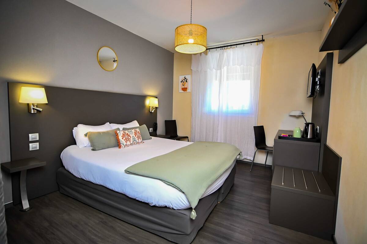 Une chambre d’hôtel moderne avec un grand lit, des lampes de chevet, un petit bureau, une télévision et une fenêtre avec des rideaux.