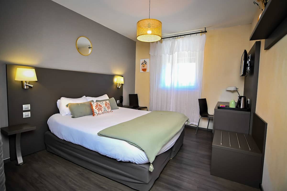 A modern hotel room with a large bed, bedside lamps, a small desk, a TV, and a window with curtains.